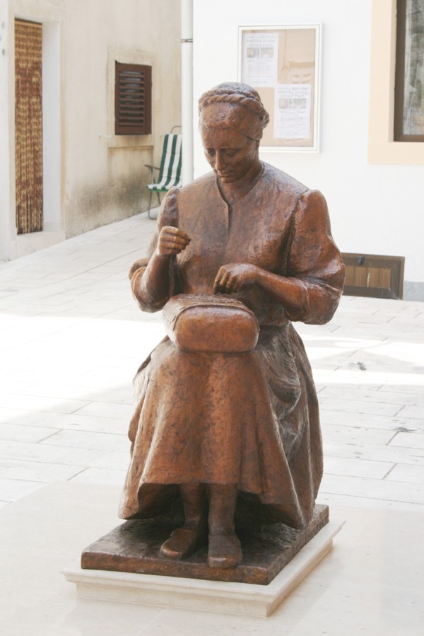 Skulptur einer Deckchen klppelnden Frau